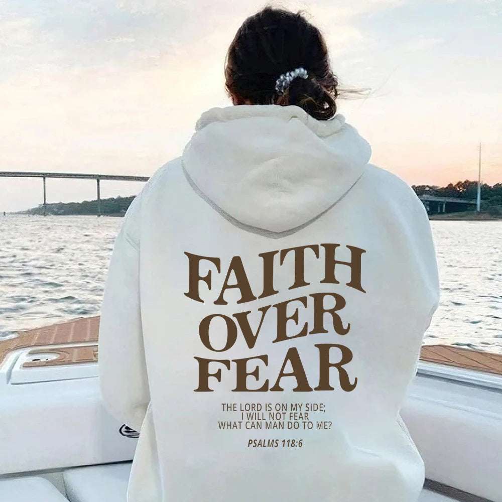 Woman wearing white Faith Over Fear hoodie with Psalm 118:6 text on back sitting on boat near water at sunset