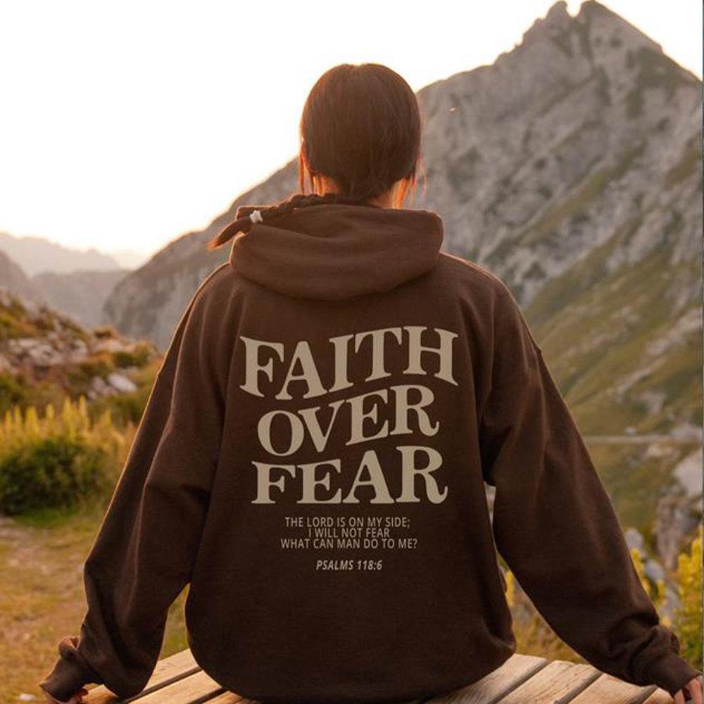 Person wearing brown Faith Over Fear Christian hoodie with mountain landscape in the background