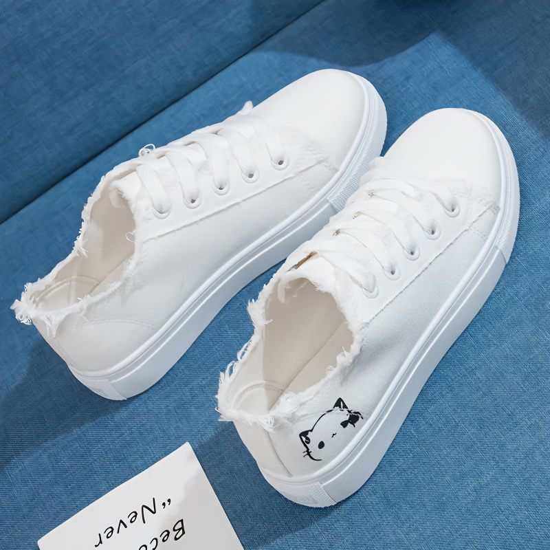 Canvas white sneakers with frayed edges and cat design on a blue fabric background