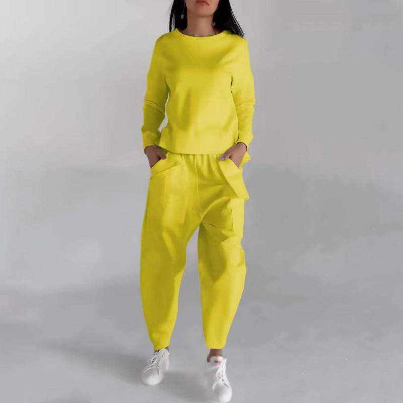 Woman wearing bright yellow fashion sweatshirt top and matching pants with white sneakers standing against a plain background