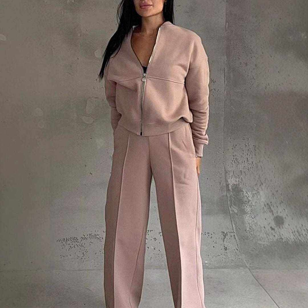 Woman wearing beige leg pants two-piece set with zip-up jacket and wide-leg pants against gray textured wall background