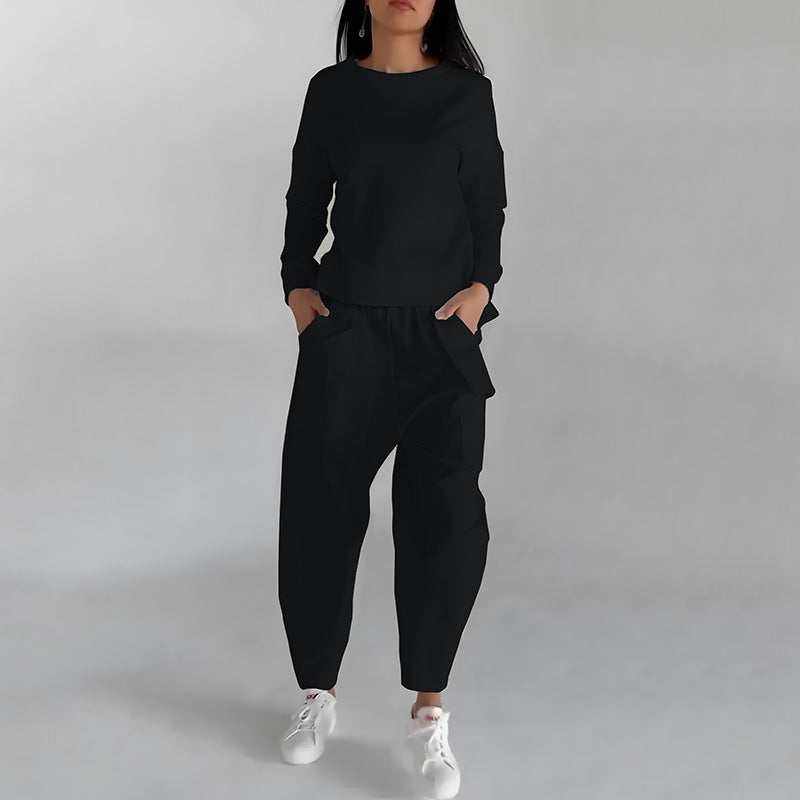 Woman wearing a black fashion sweatshirt top and matching black pants with white sneakers on a light gray background