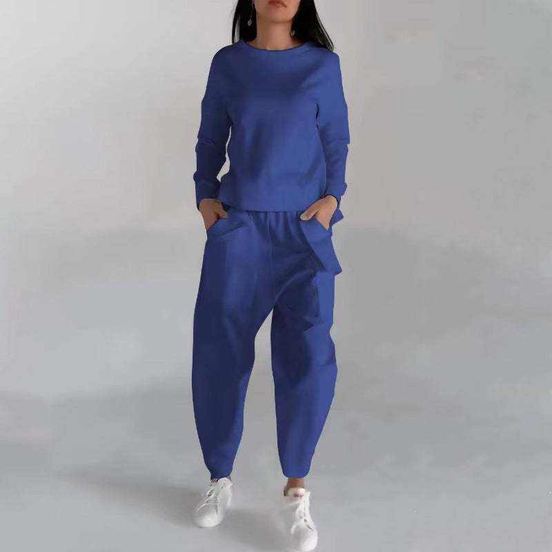 Woman wearing a blue fashion sweatshirt top and matching pants with white sneakers against a plain background