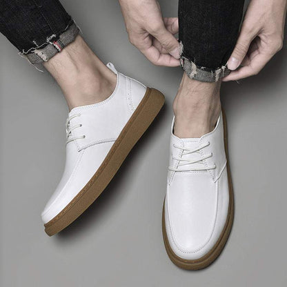 White cowhide sneakers with brown soles worn with rolled-up black jeans on a gray background