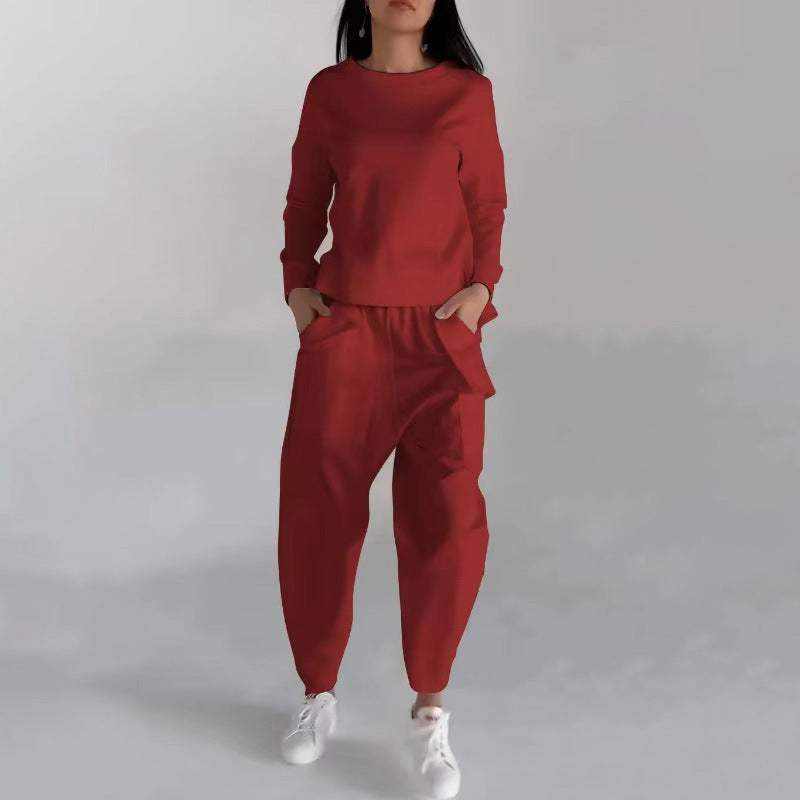 Woman wearing a red fashion sweatshirt top and matching pants with white sneakers standing against a light gray background